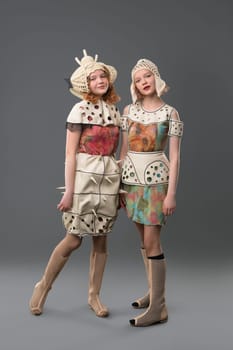 Two girls wearing fashion colorful dresses view against gray wall