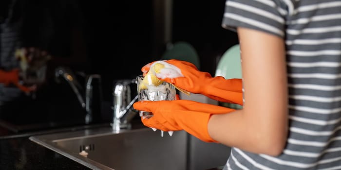 Focused young woman cleaning a soapy glass in her kitchen, demonstrating her commitment to hygiene and cleanliness in daily tasks.