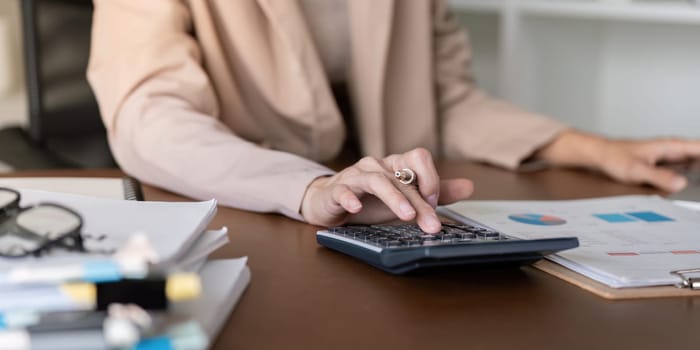 A skilled accountant diligently working on financial calculations using a calculator while reviewing reports and charts on their desk in a modern office.