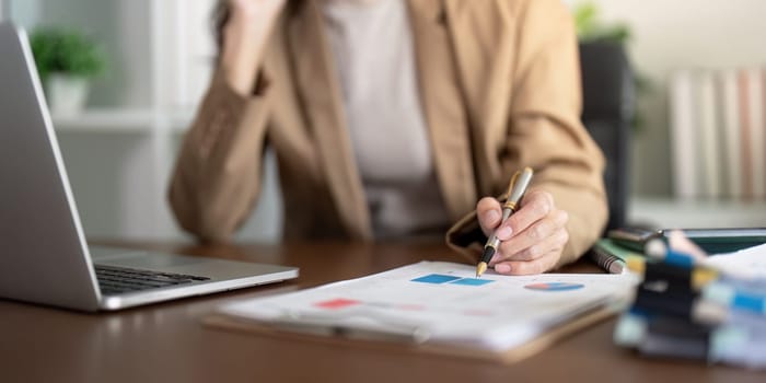 A businesswoman reviewing important financial data and charts on a clipboard at her modern office desk, showcasing analytical skills and concentration.