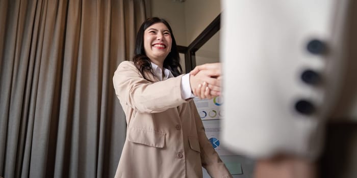 A happy female professional smiling during a handshake, celebrating a successful business agreement after a collaborative meeting in a contemporary office space.