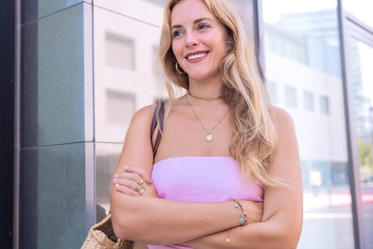 A blonde woman standing confidently with arms crossed, wearing a trendy summer outfit. Captured in an urban setting with a casual and fashionable vibe, showcasing modern elegance.