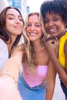 Three young women sitting outdoors, smiling, and taking a playful selfie together. Perfect for concepts like friendship, happiness, social media, and outdoor lifestyle.