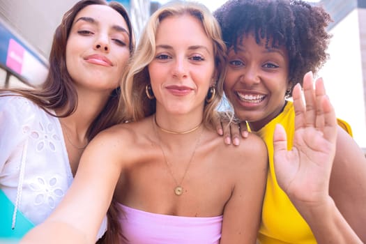 Three young women sitting outdoors, smiling, and taking a playful selfie together. Perfect for concepts like friendship, happiness, social media, and outdoor lifestyle.