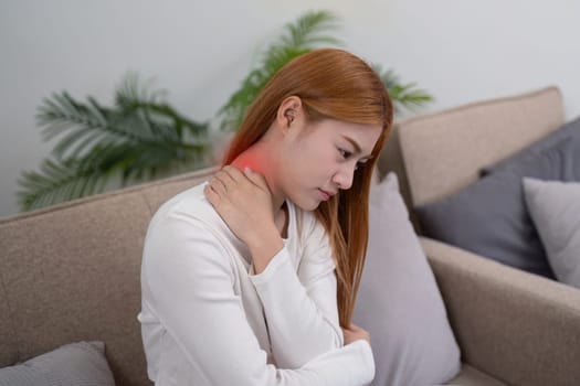 A young woman seated on a sofa, holding her shoulder in discomfort, emphasizing the importance of self-care and wellness in her personal living space.