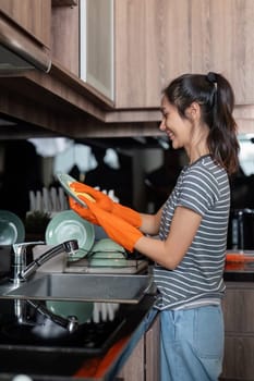 Cheerful young woman washing dishes in her kitchen sink, demonstrating a positive attitude towards her household chores.