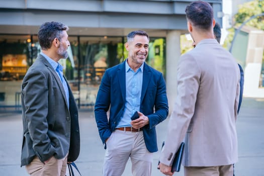 Group of four businessmen in formal and smart casual attire discussing outdoors in a modern urban setting, demonstrating teamwork and collaboration.