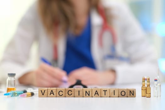 A healthcare professional emphasizes the importance of vaccination with vials and blocks spelling 'VACCINATION'.