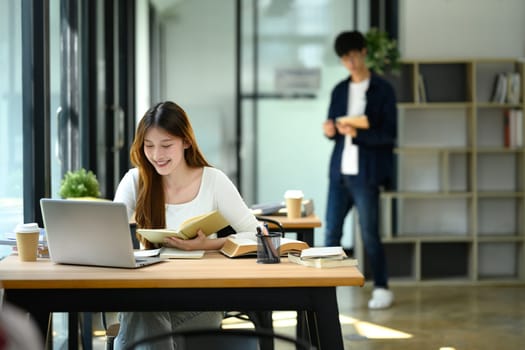 Smiling female student using laptop studying in a bright workspace.
