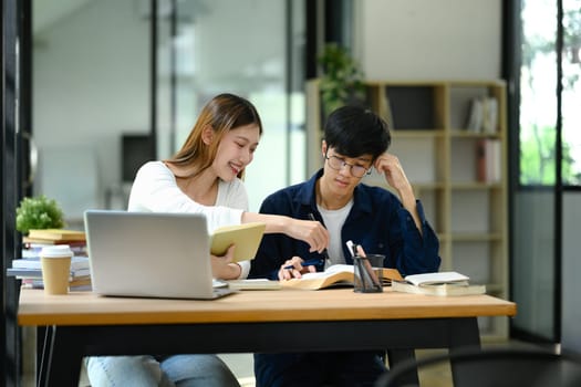 Two university students sharing ideas while studying together in a library. Education concept.