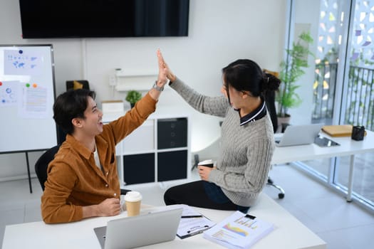 Cheerful coworkers giving high five to each other celebrating team success in a modern office.