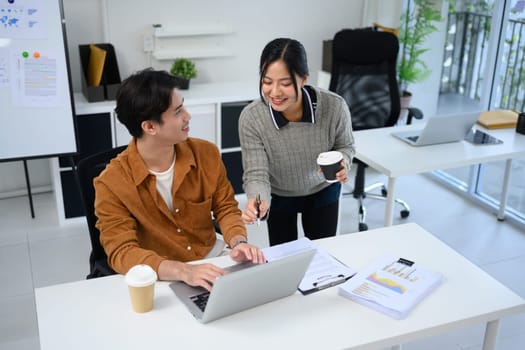 Smiling female colleague sharing ideas over laptop with her coworker in the office.