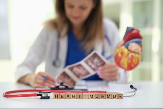 A qualified doctor examines heart images and models, focusing on diagnosing heart murmurs in a medical setting