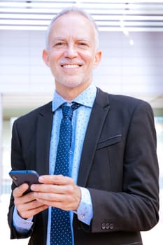 Satisfied with the results, the businessman walks on the street outside the office building, a mature boss holds a phone in his hands, writes messages and reads news online, using an application.
