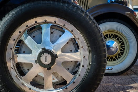 Lisbon, Portugal - Sep 29, 2024: Vintage car wheels on cobblestone road. Wheel design, wire wheel with white wall rubber tyre, chrome polished center hub cap and traditional spokes, cast aluminum racing wheel with central locking hub, 6-spoke design