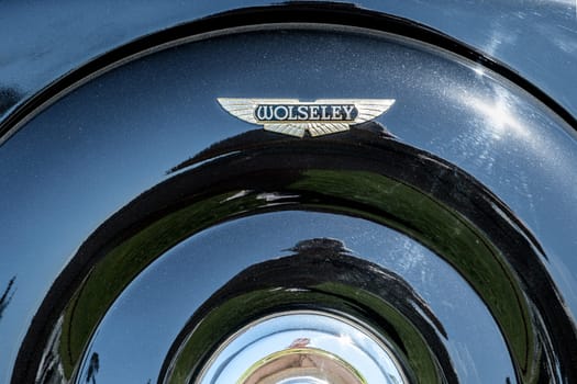 Lisbon, Portugal - Sep 29, 2024: Close-up of vintage Wolseley car spare wheel cover, metal case and Wolseley winged logo badge on sunny day. Sunlight, sun flares, reflections on clean black polished surface. Wolseley, UK