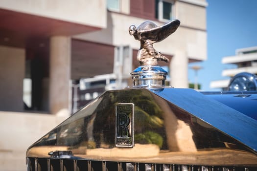 Lisbon, Portugal - Sep 29, 2024: Close-up and selective focus on the Rolls-Royce mascot hood ornament or bonnet badge called Spirit of Ecstasy, female in billowing cloth like wings behind, leaning forward, and emblem on grille. Rare kneeling version