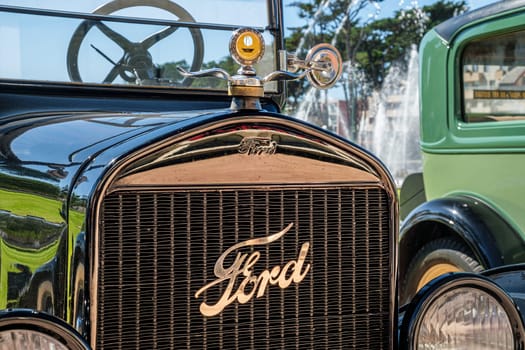Lisbon, Portugal - Sep 29, 2024: Close-up and selective focus on the Boyce MotoMeter on top of hood or bonnet and Ford emblem and logo plate on grille, Ford model T, sunny day, clear blue sky. Ford Motor Company, USA