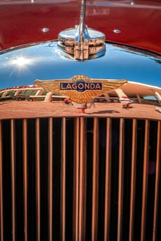 Lisbon, Portugal - Sep 29, 2024: Close view of chrome front grille, hood logo badge and radiator cap of vintage red Lagonda LG45 on sunny day. Selective focus, logo and badge of luxury sports car of 1930s, 2-door drophead coupe version, Lagonda, UK