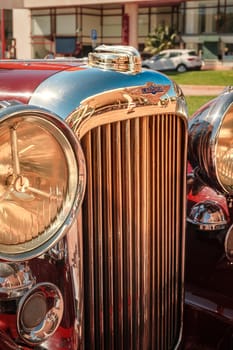 Lisbon, Portugal - Sep 29, 2024: Close view of front grille, headlights and hood of vintage red Lagonda LG45 on sunny day. Selective focus, logo and badge of luxury sports car of 1930s, 2-door drophead coupe version, Lagonda, UK