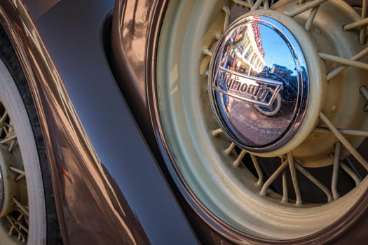 Lisbon, Portugal - Sep 29, 2024: Close-up and selective focus of spare wire wheel and wheel center cap with Plymouth logo on sunny day. Urban setting reflections, vintage look. Plymouth Chrysler motors, Chrysler Corp, USA