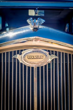 Lisbon, Portugal - Sep 29, 2024: Close-up of Wolseley logo badge and grille and bonnet badge or hood ornament in form of winged W letter in selective focus on sunny day. Sun flares on chrome details of British pre-war car, Wolseley, UK.