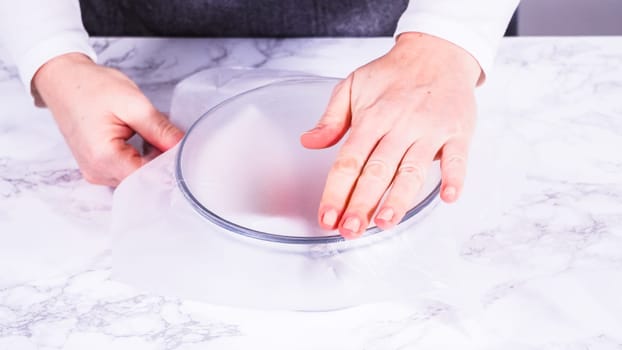 Strawberries, freshly washed and dried, are neatly stored in a glass bowl lined with a paper towel and securely covered with plastic wrap to maintain freshness.