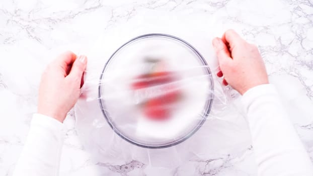 Flat lay. Strawberries, freshly washed and dried, are neatly stored in a glass bowl lined with a paper towel and securely covered with plastic wrap to maintain freshness.