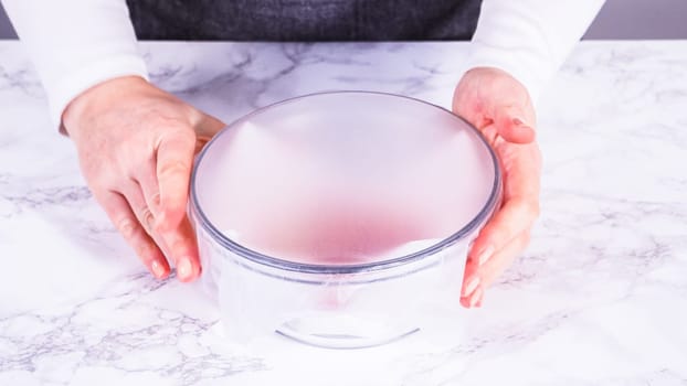 Strawberries, freshly washed and dried, are neatly stored in a glass bowl lined with a paper towel and securely covered with plastic wrap to maintain freshness.