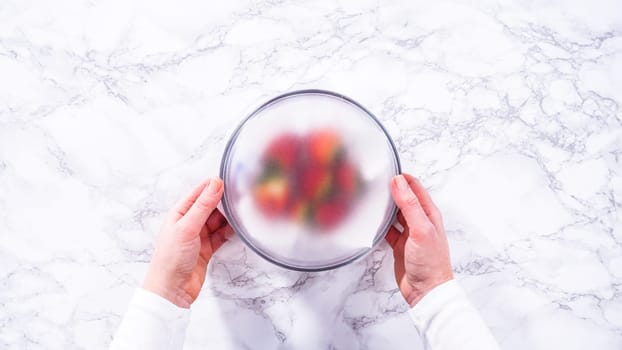 Flat lay. Strawberries, freshly washed and dried, are neatly stored in a glass bowl lined with a paper towel and securely covered with plastic wrap to maintain freshness.
