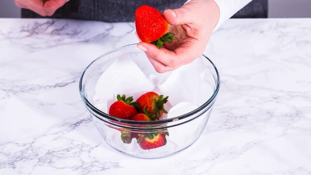 Strawberries, freshly washed and dried, are neatly stored in a glass bowl lined with a paper towel and securely covered with plastic wrap to maintain freshness.