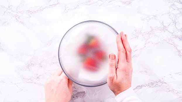 Flat lay. Strawberries, freshly washed and dried, are neatly stored in a glass bowl lined with a paper towel and securely covered with plastic wrap to maintain freshness.