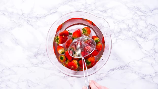 Flat lay. Ripe strawberries are submerged in water within a large glass mixing bowl, a step in washing the fruit to ensure cleanliness and longevity before storage or consumption.