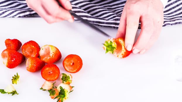 Succulent red strawberries, some showing early spoilage, are arrayed on a white cutting board, held securely in place, with a paper towel lined glass bowl nearby suggesting an attempt at preservation.
