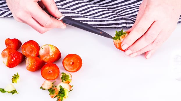 Succulent red strawberries, some showing early spoilage, are arrayed on a white cutting board, held securely in place, with a paper towel lined glass bowl nearby suggesting an attempt at preservation.