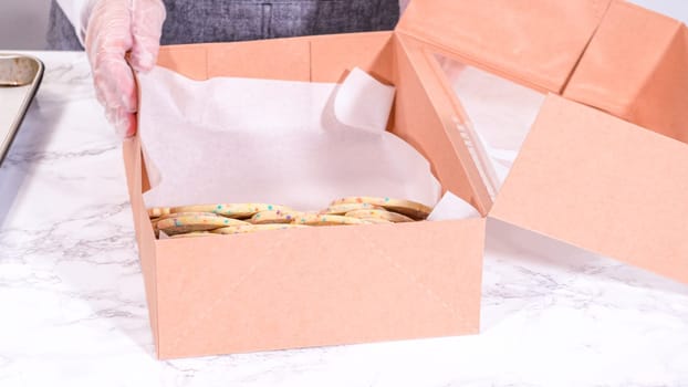 The sugar cookies, filled with sprinkles mixed into the dough, are carefully arranged with meticulous precision into a rustic brown paper box.