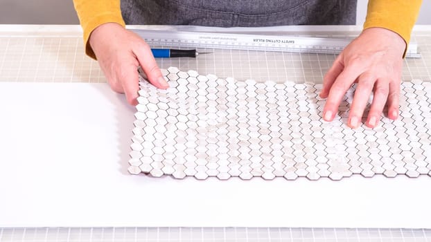 In the process of mounting peel and stick mosaic tiles onto a foam board, perfect for enhancing a food photography studio's aesthetic.