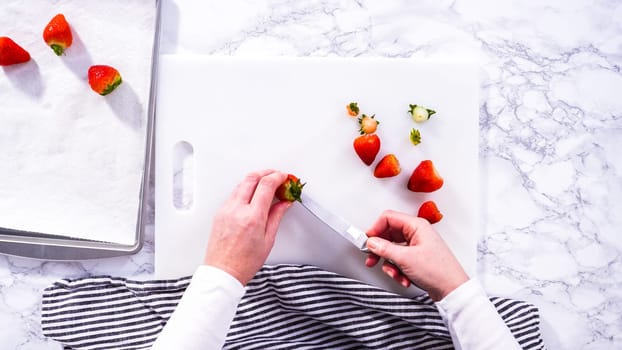 Flat lay. Succulent red strawberries, some showing early spoilage, are arrayed on a white cutting board, held securely in place, with a paper towel lined glass bowl nearby suggesting an attempt at preservation.