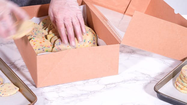 The sugar cookies, filled with sprinkles mixed into the dough, are carefully arranged with meticulous precision into a rustic brown paper box.