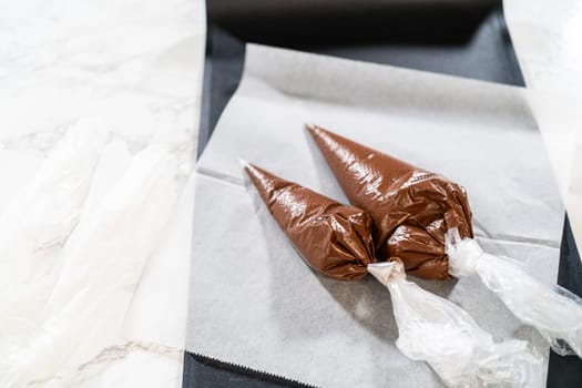Filled Piping Bags with Chocolate Icing Description: Close-up view of two piping bags filled with chocolate royal icing, placed on a white tray, prepared for decorating cookies.