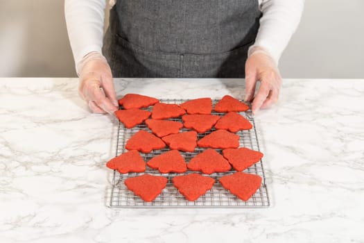 A cooling rack filled with red, tree-shaped gingerbread cookies, freshly baked and arranged in rows. These Red Gingerbread Cookies are cooling on the counter, showcasing their vibrant color and festive shapes.