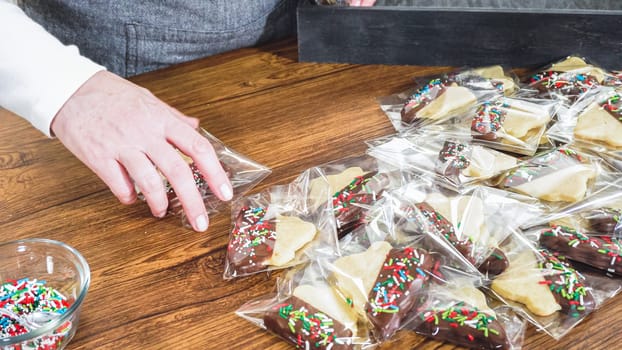 Carefully packaging Christmas cutout cookies, half-dipped in chocolate and presented in clear cellophane wrapping, perfect for festive gifting.