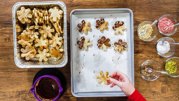 Flat lay. Creating snowflake-shaped cutout sugar cookies, dipped in chocolate, and adorned with different toppings.