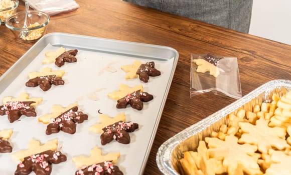 Carefully packaging Christmas cutout cookies, half-dipped in chocolate and presented in clear cellophane wrapping, perfect for festive gifting.