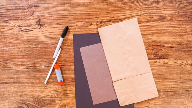 Step by step. Flat lay. Teacher guides online class through making a paper puppet from a brown bag, creatively using a wooden surface as a workspace.
