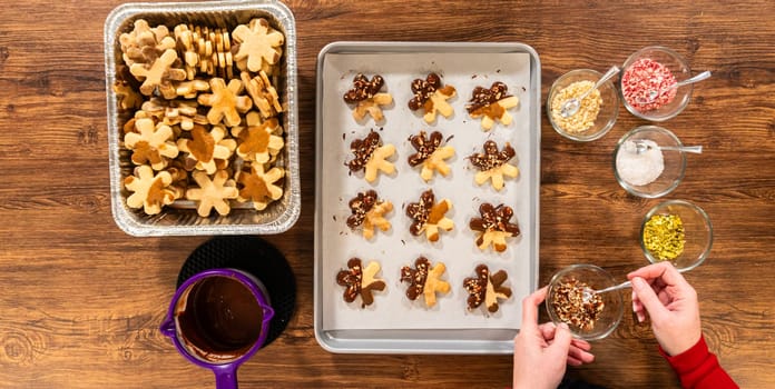 Creating snowflake-shaped cutout sugar cookies, dipped in chocolate, and adorned with crushed pecan nuts, elegantly presented on parchment.