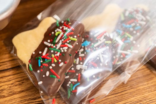 Carefully packaging Christmas cutout cookies, half-dipped in chocolate and presented in clear cellophane wrapping, perfect for festive gifting.
