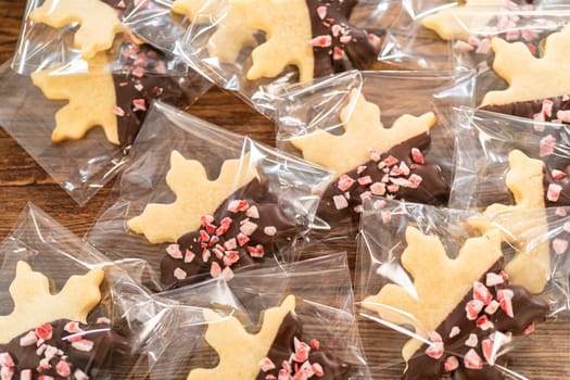 Carefully packaging Christmas cutout cookies, half-dipped in chocolate and presented in clear cellophane wrapping, perfect for festive gifting.