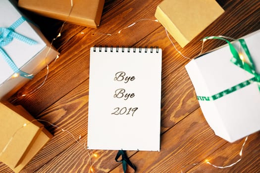 Prepare for Christmas with Notepad and gifts. Notebook with the words Bye Bye 2019 lies on a wooden table.