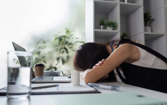 A young female office worker appears tired, resting her head on her desk in a modern office setting.